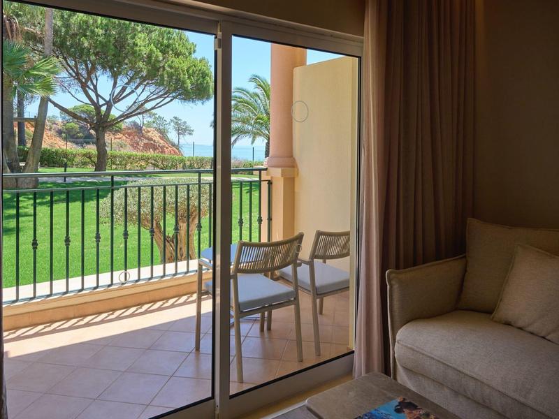 Balkon mit Stühlen, Blick auf Garten und Meer, gemütliches Sofa im Zimmer.