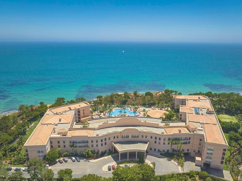 Helles Hotelzimmer mit zwei Betten und Terrasse mit Blick auf den Pool.