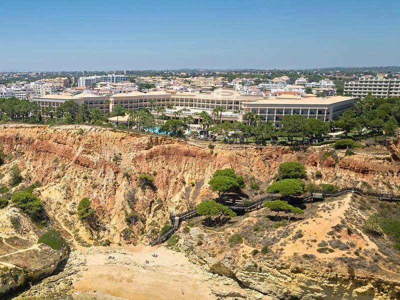 Kleiner Sandstrand mit Felsen und Hotelgebäuden im Hintergrund unter klarem Himmel.