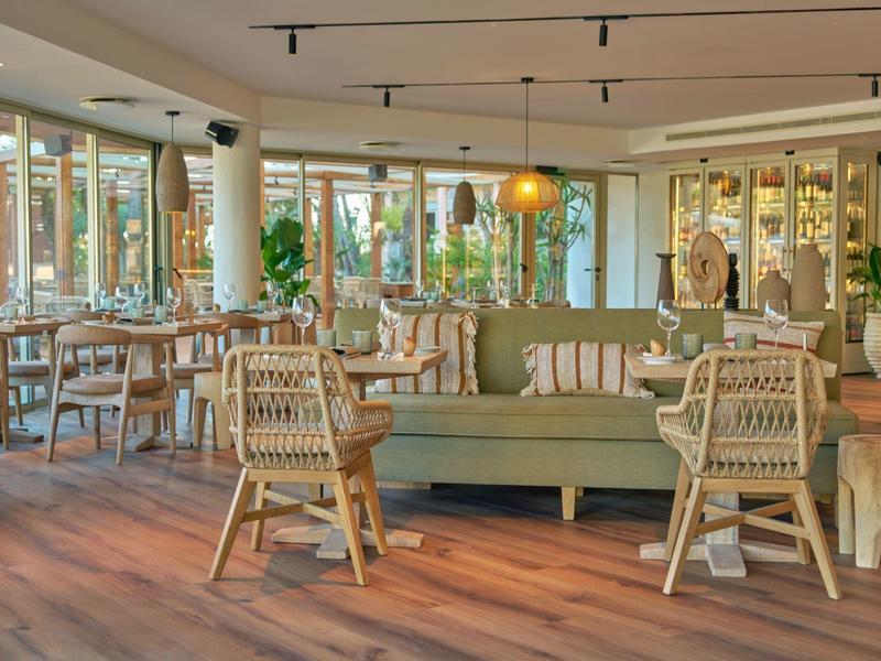 Helles Restaurant mit Holzfußboden, Stühlen aus Rattan und grünen Sofas.