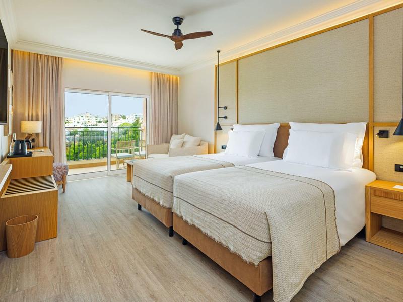 Helles Hotelzimmer mit zwei Einzelbetten, Balkon und modernem Interieur.