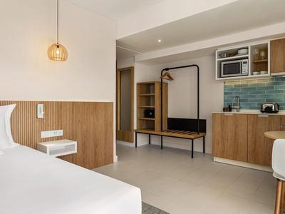 Moderner Hotelzimmer-Interior mit Holzdetails, Küchenzeile, weißen Wänden und schlichtem Design.