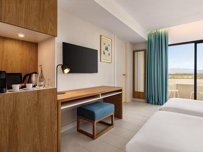 Modernes Hotelzimmer mit Holzmöbeln, TV, Schreibtisch, blauen Vorhängen und Balkon mit Weitblick.