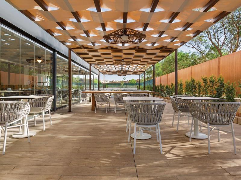Außenbereich mit Holzboden und weißen Stühlen unter einem Holz-Deckendach mit Beleuchtung.
