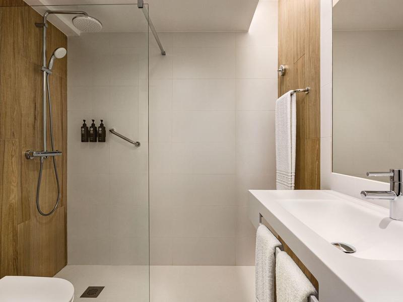 Modernes Badezimmer mit begehbarer Dusche, weißen Wänden und Holzverkleidung an einer Wand.