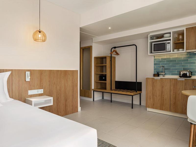 Moderner Hotelzimmer-Interior mit Holzdetails, Küchenzeile, weißen Wänden und schlichtem Design.