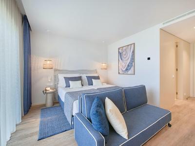 Helles Schlafzimmer mit blauem Sofa, großem Bett, Vorhängen und minimalistischer Wanddekoration.