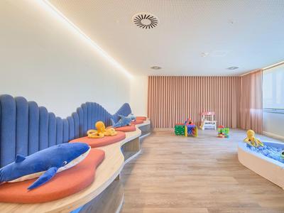 Heller Kinderspielraum mit bunten Sitzflächen, weichen Spielzeugen und großem Fenster.