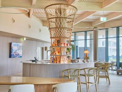 Moderner Gastraum mit Holzdecke, runder Bar und Sitzmöbeln in hellen Naturtönen.