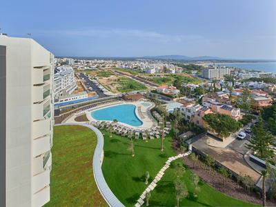 Blick auf eine Stadt mit einem großen Pool, grünen Rasenflächen und mehreren Gebäuden bei klarem Himmel.