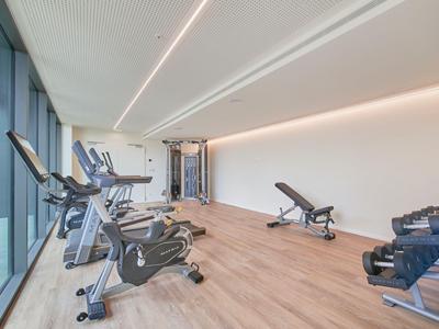 Moderner Fitnessraum mit Cardio-Geräten, Hantelbank und Kurzhanteln neben großen Fenstern.