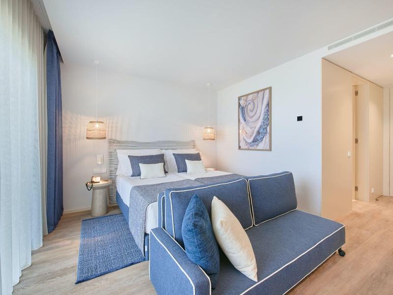 Helles Schlafzimmer mit blauem Sofa, großem Bett, Vorhängen und minimalistischer Wanddekoration.