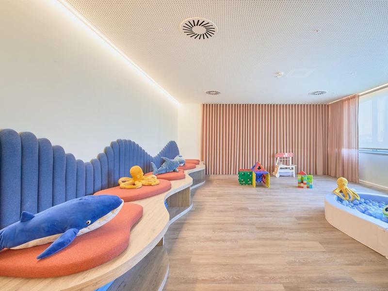 Heller Kinderspielraum mit bunten Sitzflächen, weichen Spielzeugen und großem Fenster.