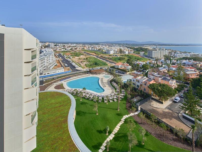 Blick auf eine Stadt mit einem großen Pool, grünen Rasenflächen und mehreren Gebäuden bei klarem Himmel.