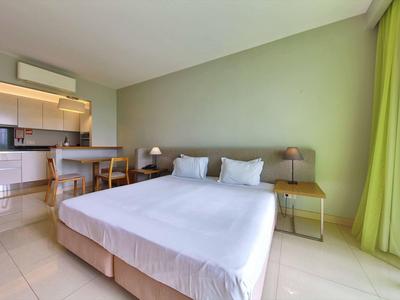 Helles Schlafzimmer mit Doppelbett, grüner Wand und angrenzender offener Küche.