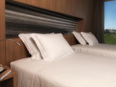 Modernes Hotelzimmer mit zwei Einzelbetten, weißen Bettlaken und Blick auf eine grüne Landschaft.