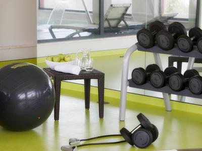 Fitnessraum mit Gymnastikball, Hanteln, Widerstandsband und Tisch mit Wasser und Äpfeln.
