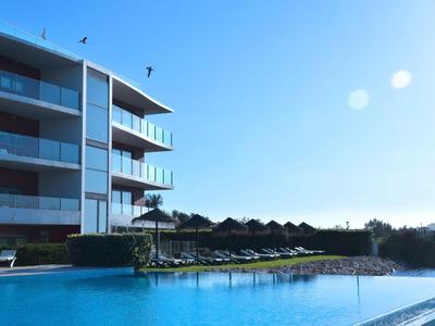 Moderner Hotelkomplex mit großem Pool und Liegestühlen bei klarem blauem Himmel.