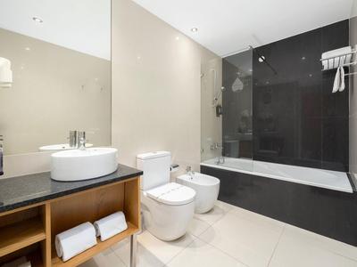 Modernes Badezimmer mit Waschbecken, Toilette, Bidet und Badewanne mit Glaswand.