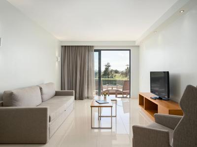Modernes Wohnzimmer mit Sofa, Sesseln, TV und Balkonblick in einem Hotelzimmer.