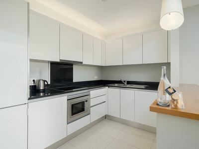 Moderne, helle Küchenzeile mit weißen Schränken und schwarzen Arbeitsflächen in einer Hotelwohnung.