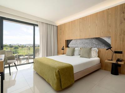 Modernes Hotelzimmer mit großem Fenster, Doppelbett, Holzverkleidung und Blick auf Terrasse.