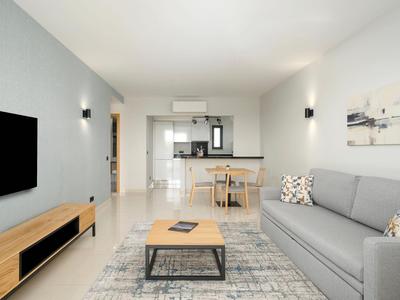 Helles Wohnzimmer mit grauem Sofa, Teppich, Holztisch und moderner Küchenzeile im Hintergrund.