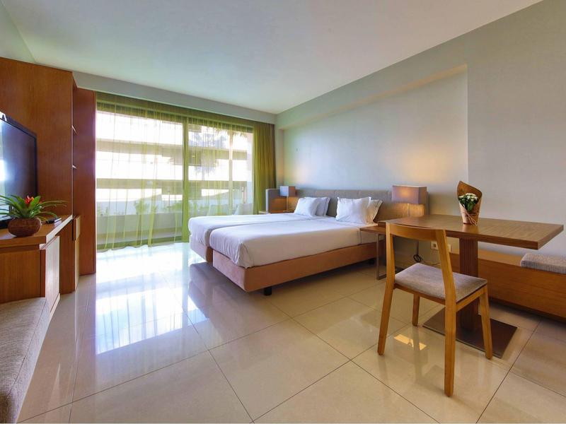 Helles Hotelzimmer mit Doppelbett, Balkon, Schreibtisch und Fernseher.