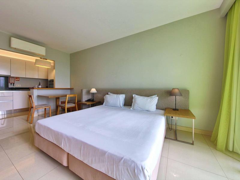 Helles Schlafzimmer mit Doppelbett, grüner Wand und angrenzender offener Küche.