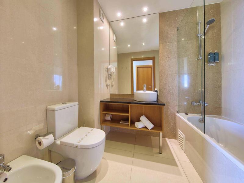 Modernes Badezimmer mit Toilette, Bidet, Waschbecken und Badewanne mit Duschabtrennung.