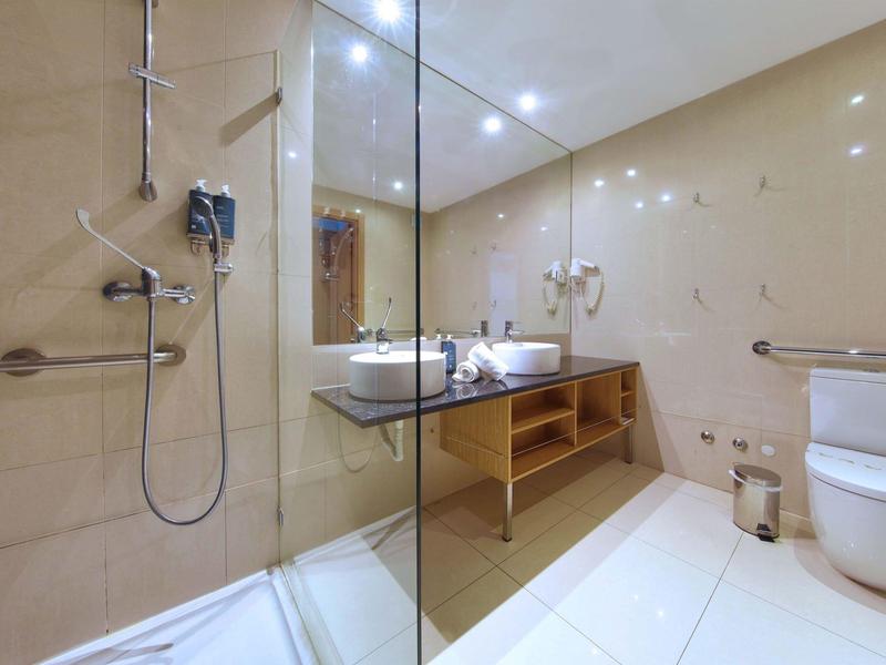 Modernes Badezimmer mit Glasdusche, Waschbecken, Föhn und Toilette in warmen Tönen