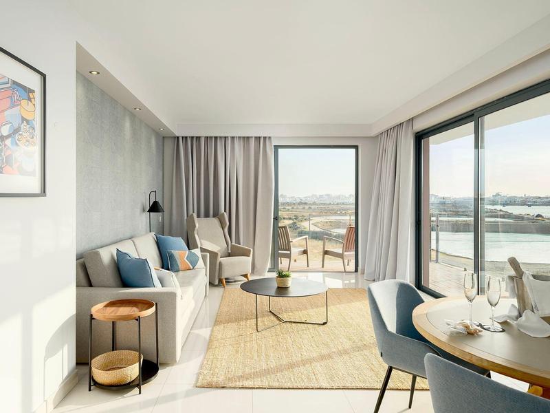 Helles Wohnzimmer mit Sofa, Sesseln, großem Fenster und Meerblick.