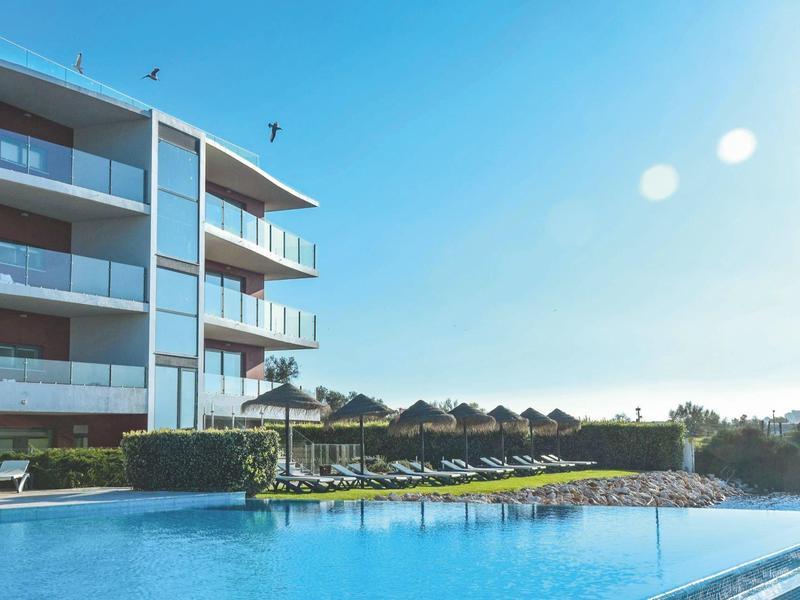 Moderner Hotelpool mit Liegestühlen und Sonnenschirmen unter klarem blauem Himmel.