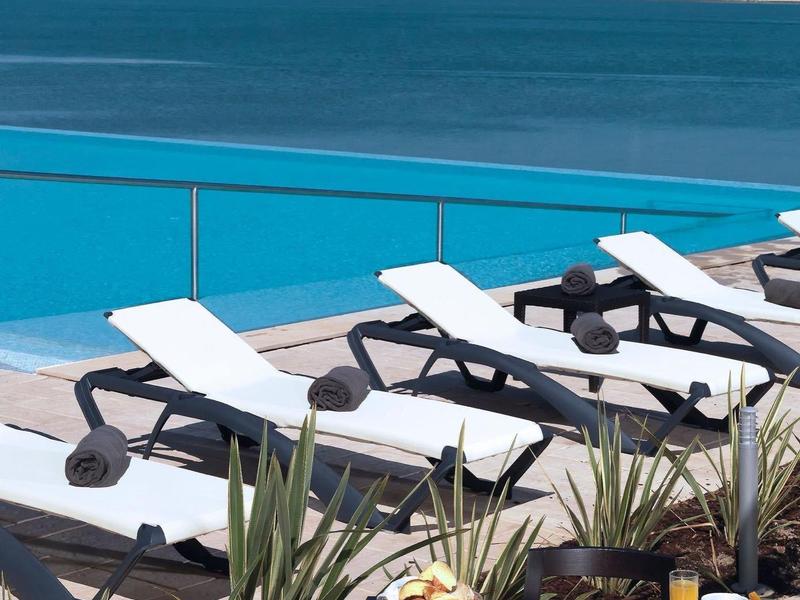 Terrasse mit Liegestühlen und gedecktem Frühstückstisch mit Blick auf das Meer und die Stadt.