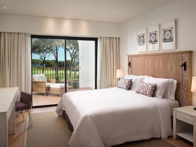 Gemütliches Schlafzimmer mit großem Bett, Holzmöbeln, Lampen und Blick auf Terrasse und See.