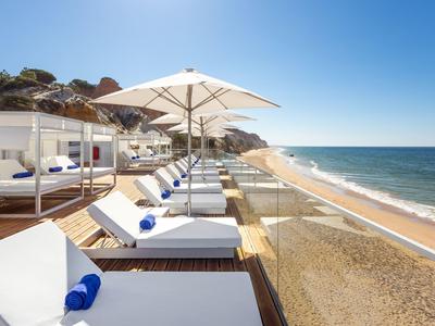 Strand mit weißen Liegen, Sonnenschirmen und klarem blauem Himmel am Meer.