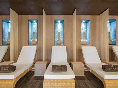 Ruhebereich mit weißen Liegen, Holzwänden und dekorativen Nischen mit blauen Glasflaschen.