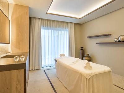 Helles Massagezimmer mit Holzschrank, Massagetisch und zwei Wandregalen mit Deko.