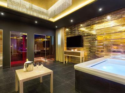 Luxuriöser Raum mit Whirlpool, goldfarbenen Wänden, TV, Glasduschen und kleinem Holztisch.