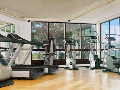 Brightly lit gym with treadmills and elliptical machines by large windows.