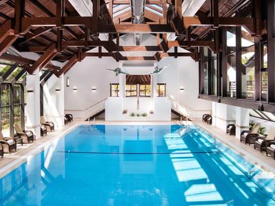 Helles Hallenbad mit blauer Wasserfläche, Holzbalken an der Decke und Sonneneinstrahlung.