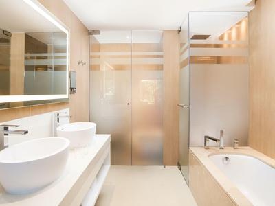 Helles Badezimmer mit zwei weißen Waschbecken, Spiegel, Badewanne und matten Glastüren.