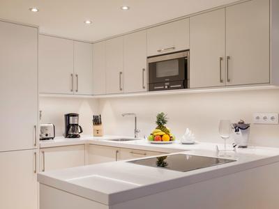 Moderne weiße Küchenzeile mit eingebautem Herd, Mikrowelle, Kaffeemaschine und Obstschale.