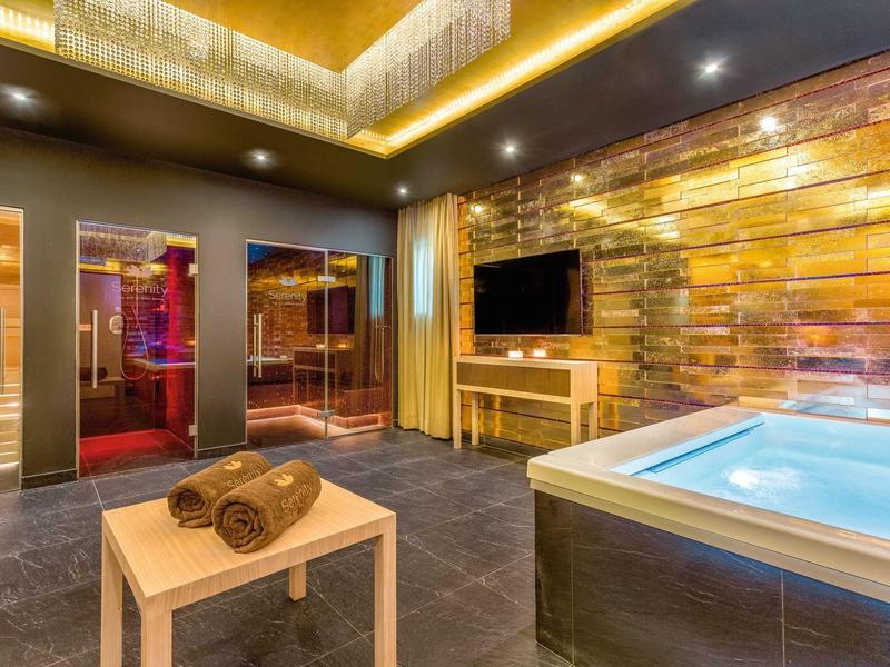 Moderner Wellnessraum mit Sauna, Whirlpool, Holztisch und warmen goldenen Farbtönen.