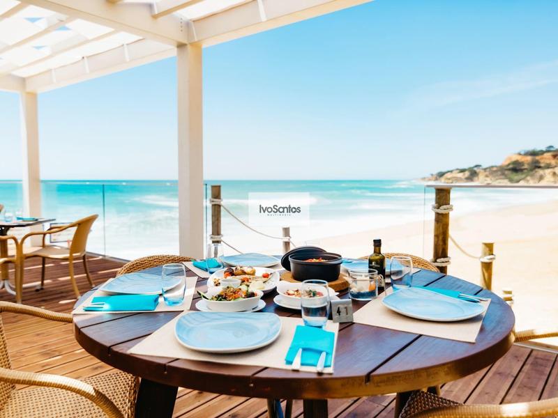 Terrasse mit gedecktem Tisch, Meerblick, heller Sonnentag, Holzstühle, Sandstrand im Hintergrund.
