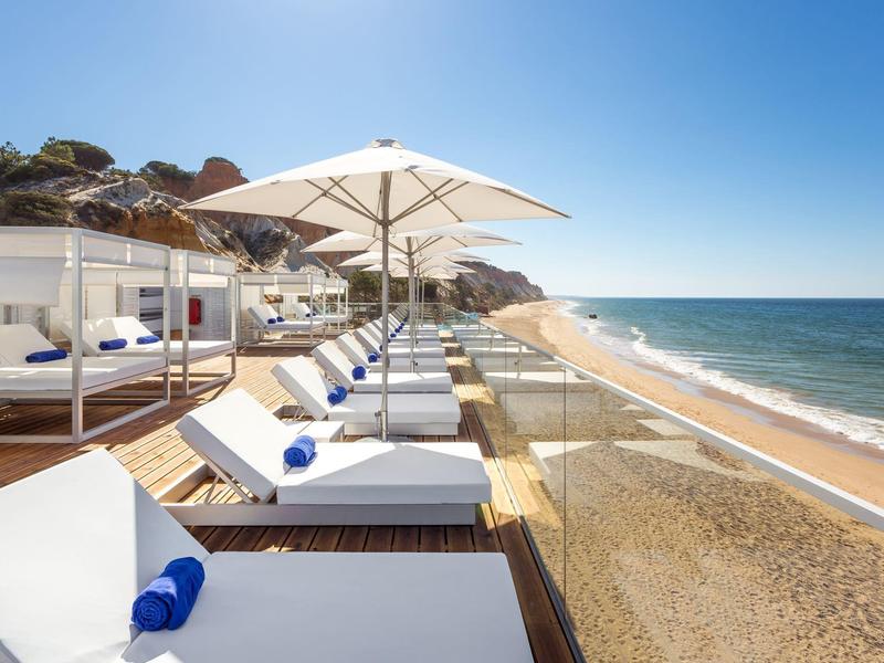Strand mit weißen Liegen, Sonnenschirmen und klarem blauem Himmel am Meer.