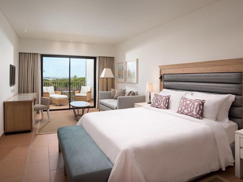 Helles Schlafzimmer mit großem Bett, Sitzbank, Nachttischlampen und Balkon mit Ausblick.