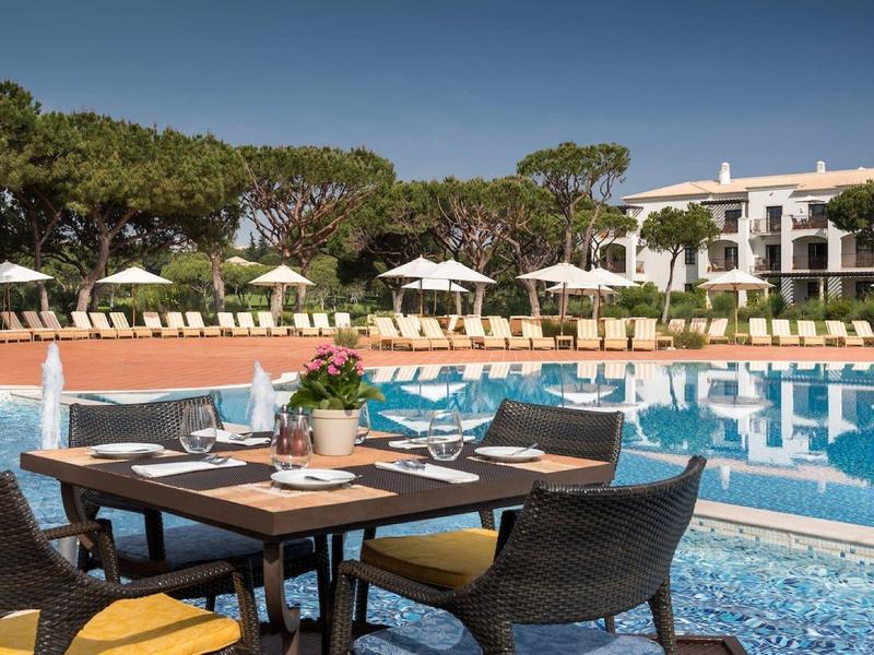 Luxuriöser Außenpool mit Sonnenliegen, Schirmen und gedecktem Tisch in einer Hotelanlage.