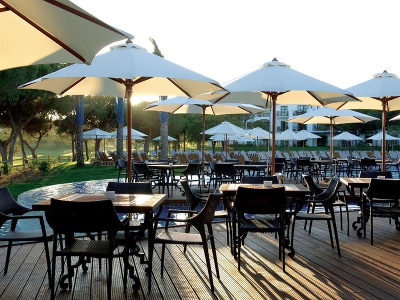 Terrasse mit schwarzen Stühlen und Tischen, vielen weißen Sonnenschirmen und Holzlattenboden.