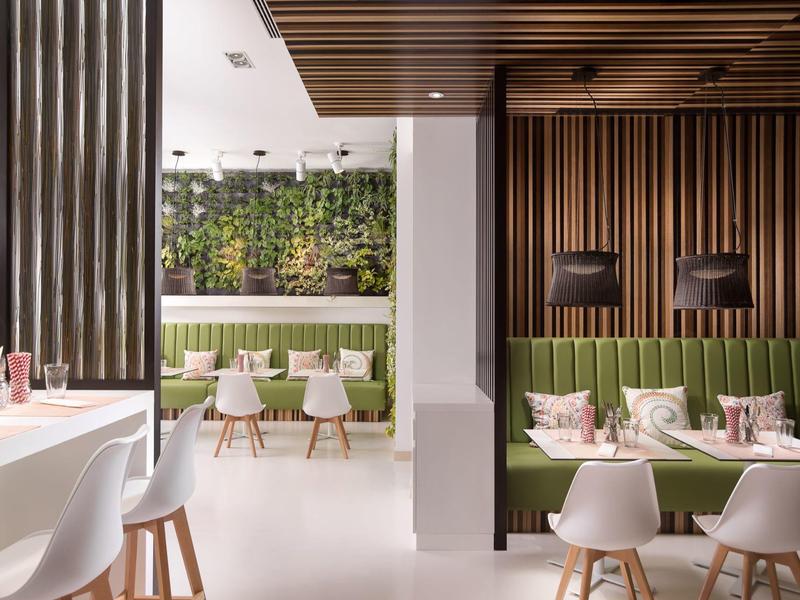 Modernes Café mit grünen Pflanzenwänden, weißen Stühlen und Holzdecken samt vertikalen Wandpaneelen.